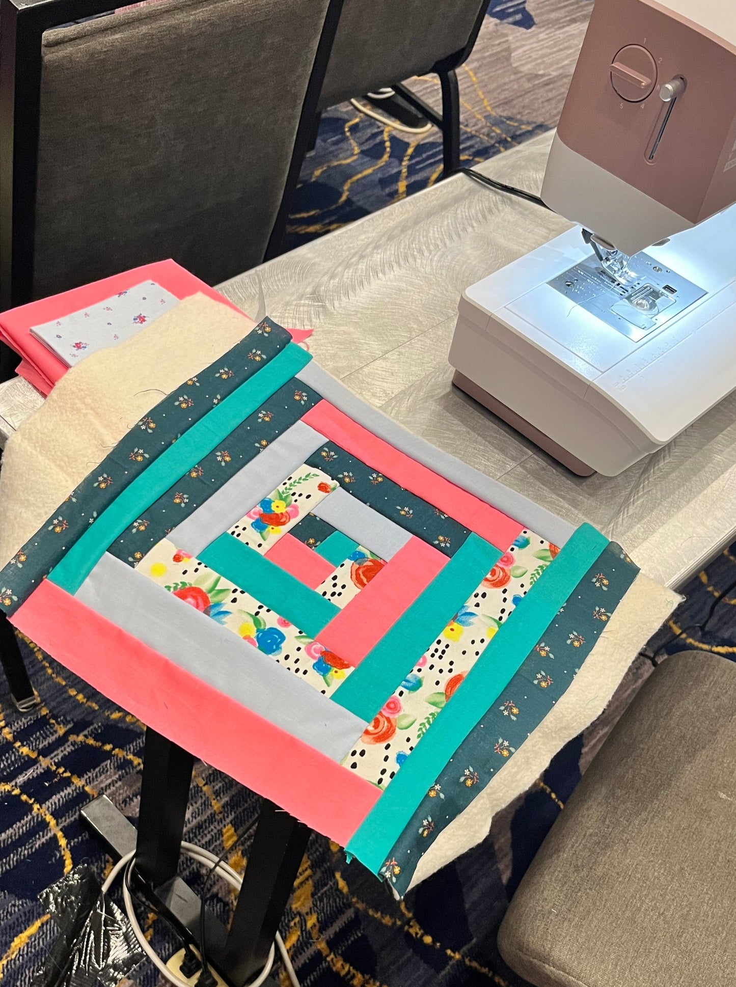 progress shot of a quilt as you go placemat in pink and green floral fabric sitting on a table next to a sewing machine