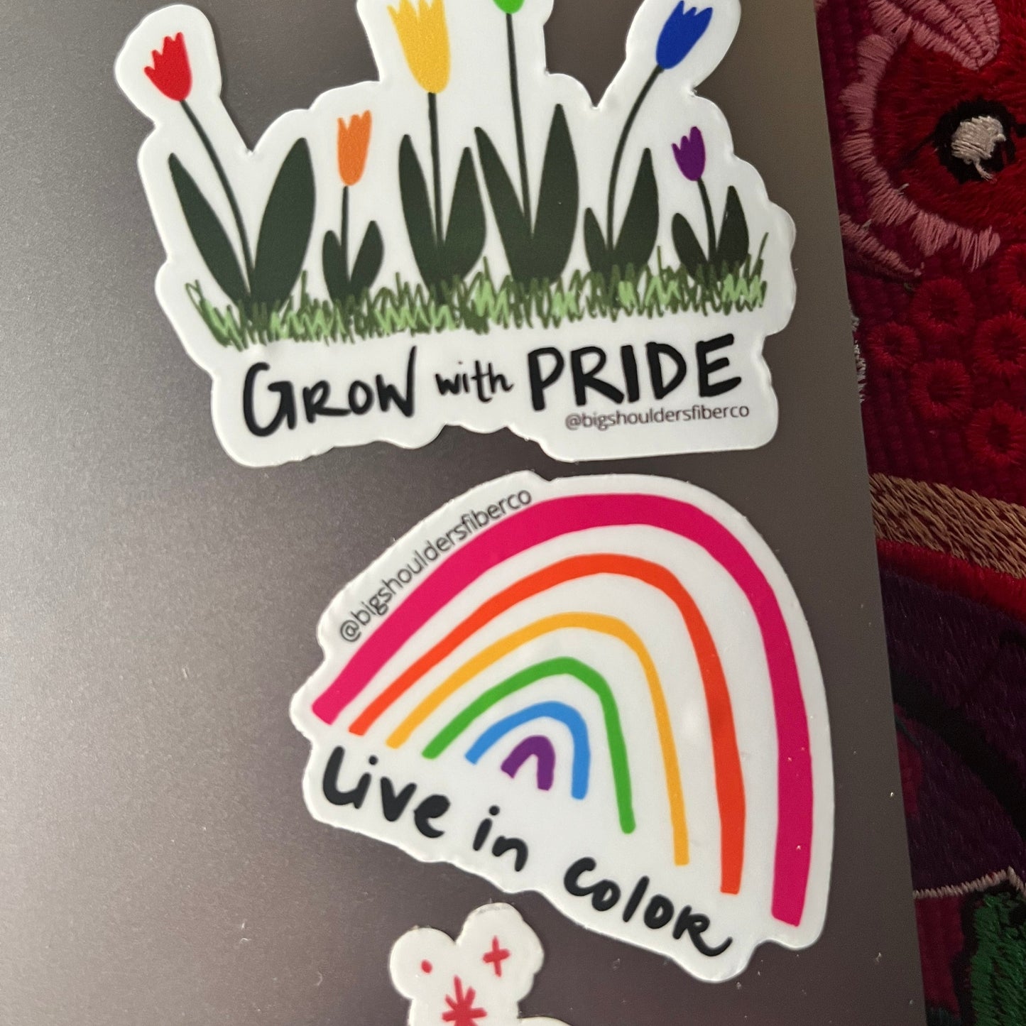 two stickers on a laptop, a hand-drawn rainbow with Live in Color, the other rainbow tulips with Grow with Pride