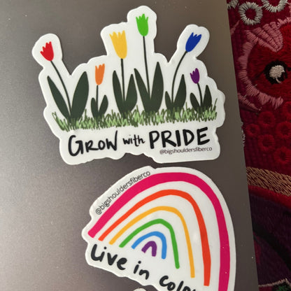 Two stickers on a laptop, one with rainbow tulips and Grow with Pride, the other a rainbow with Live in Color